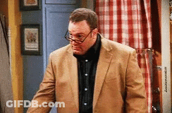 A Man Wearing Glasses And A Tan Suit Is Standing In A Room GIF