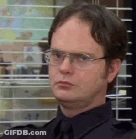 A Man Wearing Glasses And A Tie Is Sitting In Front Of A Window With Blinds . GIF