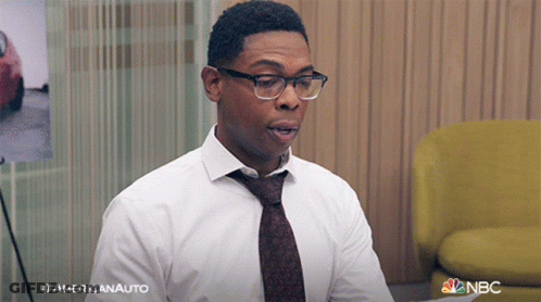 A Man Wearing Glasses And A Tie Is Sitting In Front Of A Yellow Chair .. GIF