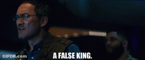 A Man Wearing Glasses And A Vest Is Standing In A Dark Room . GIF