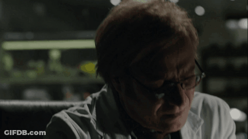 A Man Wearing Glasses And A White Coat Looks Down GIF
