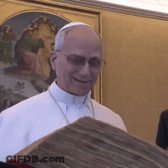 A Man Wearing Glasses And A White Robe Is Smiling While Holding A Book GIF