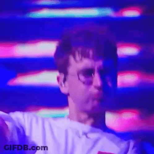 A Man Wearing Glasses And A White Shirt Is Dancing In Front Of A Purple And Pink Background . GIF