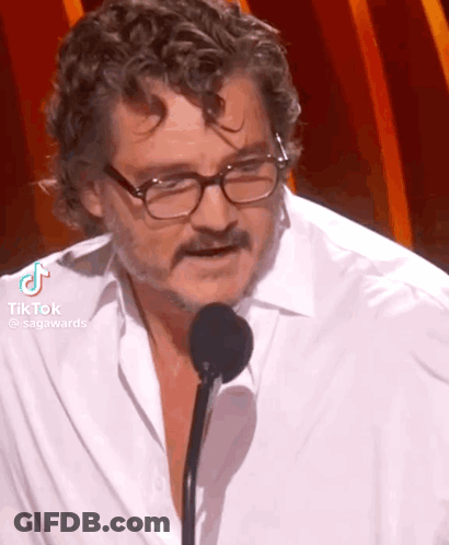 A Man Wearing Glasses And A White Shirt Is Speaking Into A Microphone . GIF