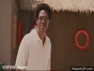 A Man Wearing Glasses And A White Shirt Is Standing In Front Of A Thatched Roof And Smiling . GIF
