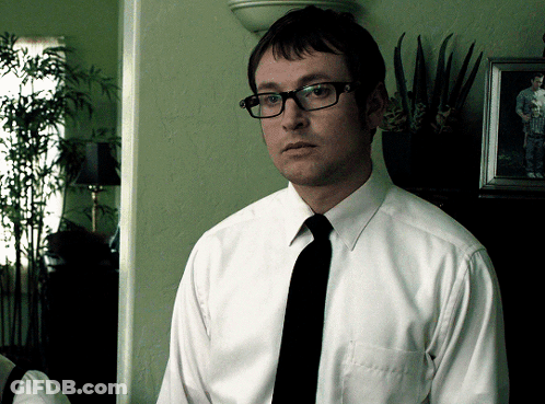 A Man Wearing Glasses And A White Shirt Stands In Front Of A Picture GIF