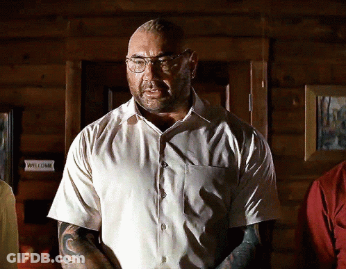 A Man Wearing Glasses And A White Shirt Stands In Front Of A Sign That Says Welcome GIF