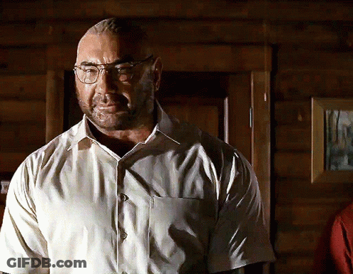 A Man Wearing Glasses And A White Shirt Stands In Front Of A Wooden Door GIF