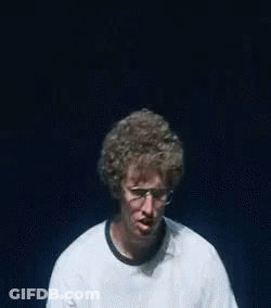 A Man Wearing Glasses And A White Shirt That Says Vote For Is Making A Funny Face . GIF