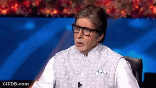 A Man Wearing Glasses And A White Vest Is Sitting In Front Of A Microphone . GIF