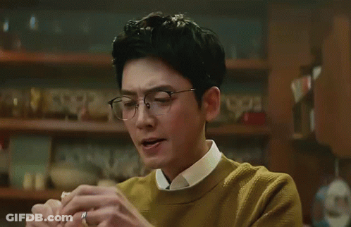 A Man Wearing Glasses And A Yellow Sweater Is Holding His Nose GIF