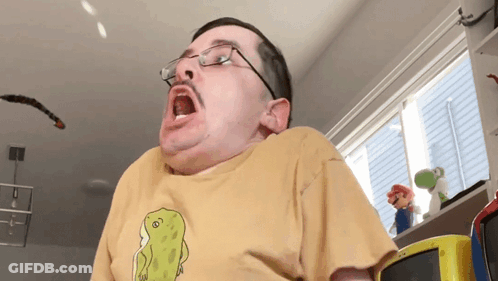 A Man Wearing Glasses And A Yellow T-Shirt With A Dinosaur On It GIF