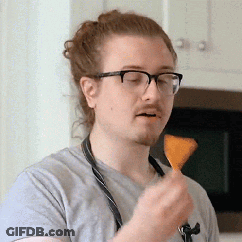 A Man Wearing Glasses And An Apron Is Eating A Chip GIF