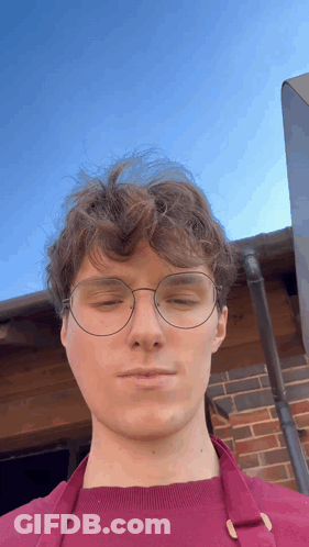 A Man Wearing Glasses And An Apron Looks At The Camera With His Eyes Closed GIF