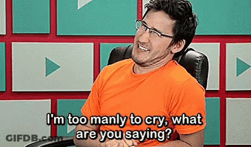 A Man Wearing Glasses And An Orange Shirt Is Sitting In A Chair And Laughing . GIF