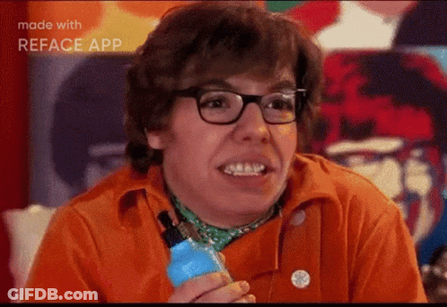A Man Wearing Glasses And An Orange Shirt Is Smiling And Holding A Blue Bottle . GIF