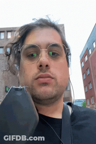 A Man Wearing Glasses And Headphones Holds A Cell Phone In Front Of His Face GIF