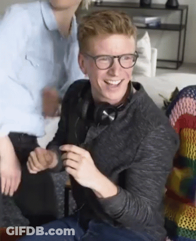A Man Wearing Glasses And Headphones Is Sitting On A Couch And Smiling . GIF