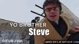 A Man Wearing Glasses And Headphones Is Standing In Front Of A Wall With Graffiti On It . GIF