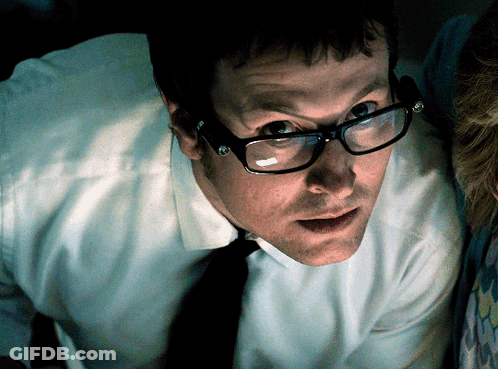 A Man Wearing Glasses And Suspenders Is Looking At Something GIF