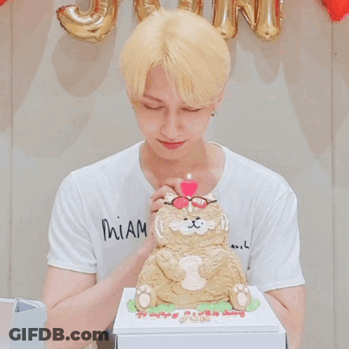 A Man Wearing Glasses Blows Out A Pink Candle On Top Of A Cat Cake GIF