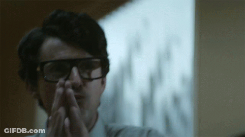 A Man Wearing Glasses Has His Hands Folded In Front Of Him GIF