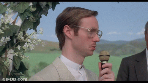 A Man Wearing Glasses Holds A Microphone In His Right Hand GIF