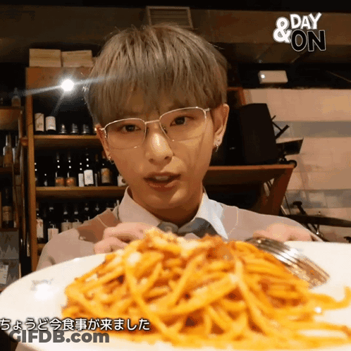 A Man Wearing Glasses Holds A Plate Of Spaghetti In Front Of A Sign That Says " Day & On " GIF