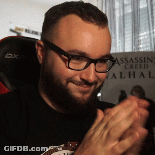 A Man Wearing Glasses Is Clapping In Front Of A Assassin Creed Valhal Poster GIF