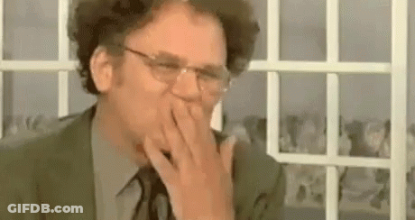 A Man Wearing Glasses Is Covering His Mouth With His Hand . GIF