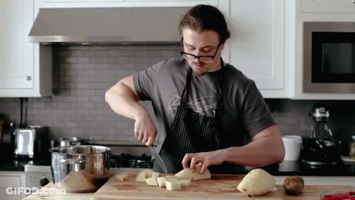 A Man Wearing Glasses Is Cutting Potatoes On A Wooden Cutting Board GIF