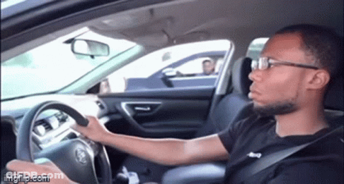 A Man Wearing Glasses Is Driving A Car And Making A Face . GIF