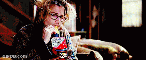 A Man Wearing Glasses Is Eating A Bag Of Doritos Chips While Sitting On A Couch . GIF