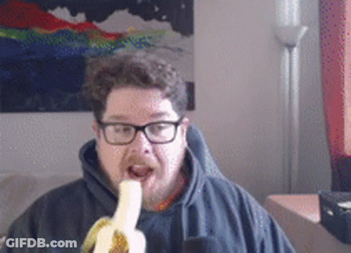 A Man Wearing Glasses Is Eating A Banana In Front Of A Painting GIF