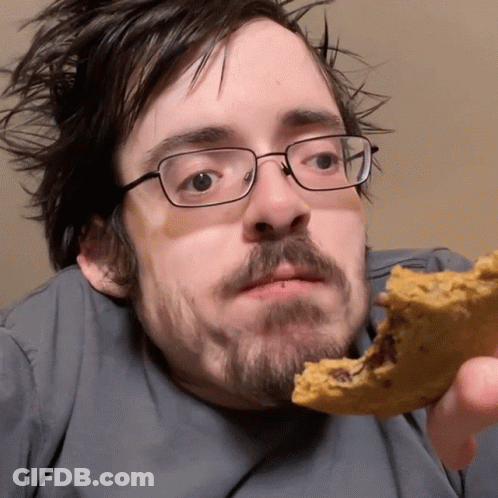 A Man Wearing Glasses Is Eating A Cookie With A Bite Taken Out Of It GIF