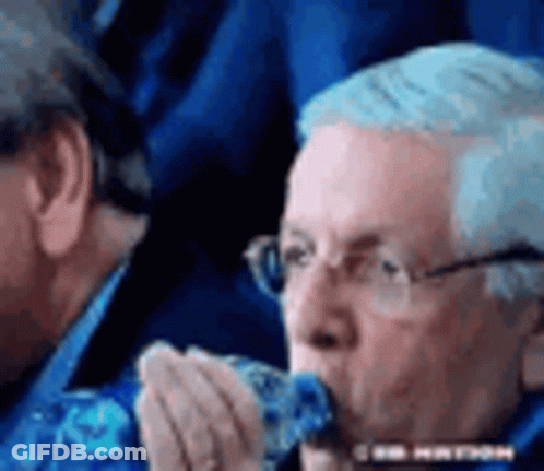 A Man Wearing Glasses Is Eating A Piece Of Food While Sitting In A Stadium . GIF