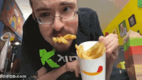 A Man Wearing Glasses Is Eating French Fries From A Cup With A Smile On It GIF