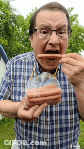 A Man Wearing Glasses Is Eating Hot Dogs From A Bag GIF