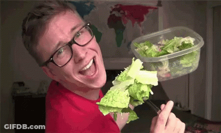 A Man Wearing Glasses Is Eating Lettuce From A Plastic Container With Chopsticks . GIF