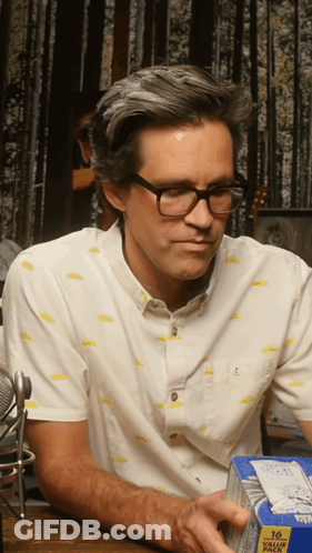 A Man Wearing Glasses Is Holding A Box Of 16 Value Pack GIF