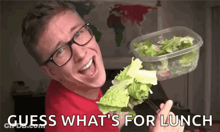 A Man Wearing Glasses Is Holding A Container Of Lettuce And A Piece Of Lettuce On A Fork . GIF