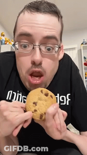 A Man Wearing Glasses Is Holding A Cookie In His Hands GIF