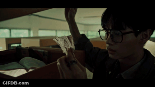 A Man Wearing Glasses Is Holding Another Man 'S Hand In A Dark Room GIF