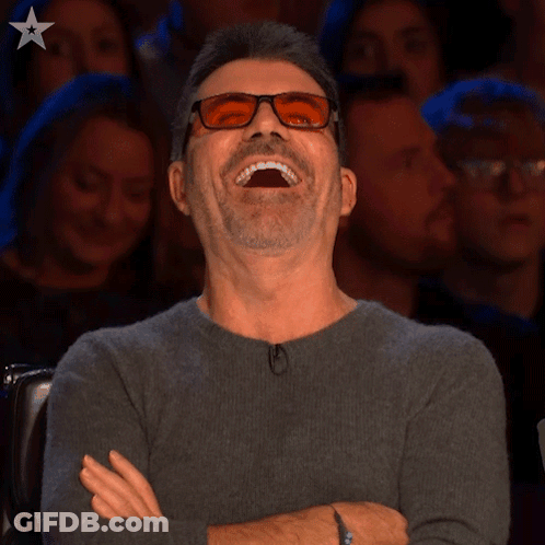 A Man Wearing Glasses Is Laughing While Sitting In Front Of A Crowd GIF