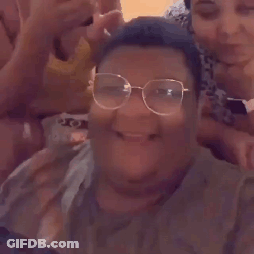 A Man Wearing Glasses Is Laughing While Taking A Selfie With His Friends . GIF