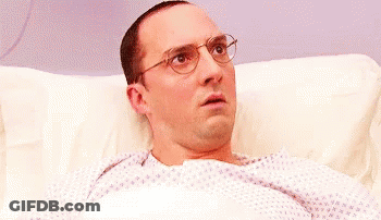 A Man Wearing Glasses Is Laying In A Hospital Bed Looking Surprised . GIF
