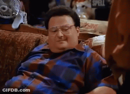A Man Wearing Glasses Is Laying On A Couch With A Fan In The Background GIF