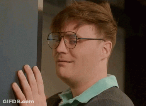 A Man Wearing Glasses Is Leaning Against A Wall With His Hand GIF