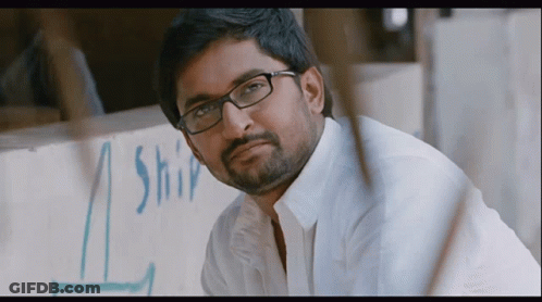 A Man Wearing Glasses Is Looking At The Camera In Front Of A Sign That Says Ship GIF