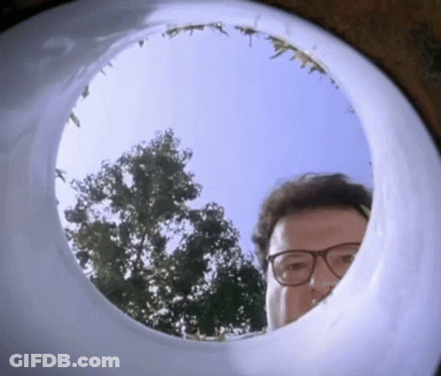 A Man Wearing Glasses Is Looking Through A Hole In A Toilet Bowl . GIF